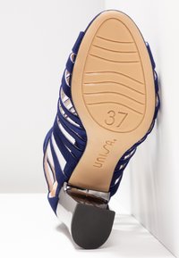 Mörkblå mocka klacksandaler med utskärningsdesign, silveraccent vid klacken, gummisula och storlek 37 markerad på undersidan.