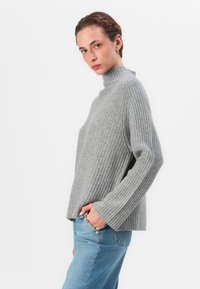 Lys grå ribbestrikket turtleneck genser laget av mykt stoff, med lange ermer og en avslappet passform, sammen med lyseblå jeans.