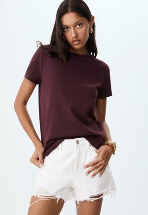 T-shirt court à manches courtes bordeaux associé à un short en denim blanc déchiré. Le t-shirt a un col rond et une coupe décontractée, mettant en avant un style casual.