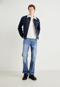 Jeans jakna z bežnim krznom, temno modra tkanina in sprednji žepi. Nosi se z svetlomodrimi kavbojkami in črnimi vezalkami.