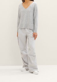 Pull en maille gris clair avec col en V, associé à un pantalon ample en nylon gris clair. Le modèle porte des baskets blanches. Texture douce évidente.
