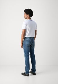 Camiseta blanca de manga corta con dobladillo curvado, combinada con jeans de mezclilla azules. El conjunto tiene un corte holgado y un diseño sencillo.