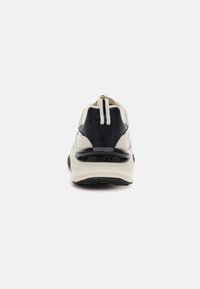 Chunky sneakers in beige en zwart met een geprofileerde achterkant, rubberen zool en een merkafdruk op de hak. Verticale strepen op de haklap voor extra detail.