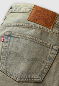 Jeans de mezclilla azul claro con un parche de cuero en la parte trasera etiquetado "Levi Strauss & Co." El bolsillo trasero presenta costuras características y una etiqueta roja.