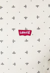 Tessuto bianco con piccoli motivi a pois neri e forme di foglie. Presenta un logo Levi's ricamato in rosso e bianco.