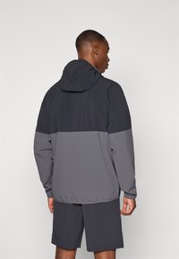 Tmavošedá mikina s kapucňou, ktorá má dvojtónový dizajn s svetlejšou šedou páskou v strede. Vyrobená z ľahkého, hladkého materiálu.