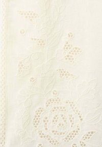 Tissu blanc délicat avec des motifs floraux brodés et des découpes semblables à de la dentelle le long des bords, mettant en valeur un savoir-faire complexe.