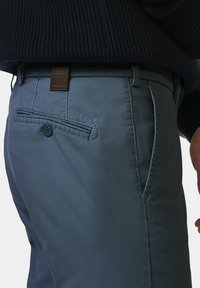 Blaue Slim-Fit-Hosen mit glatter Textur, ausgestattet mit einem Lederetikett, einem Knopfdetail an der Gesäßtasche und einem tonalen Stich.