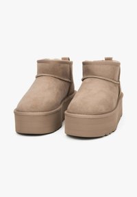 Beżowe zamszowe botki za kostkę z okrągłym noskiem, płaską podeszwą na platformie i miękką podszewką z owczej skóry, wyposażone w boczny pasek i minimalistyczne przeszycia.