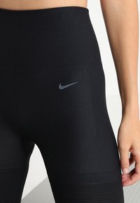 Czarne, wysokie legginsy z teksturowanymi, żebrowanymi panelami oraz małym szarym logo Nike z przodu. Elastyczny i dopasowany krój.