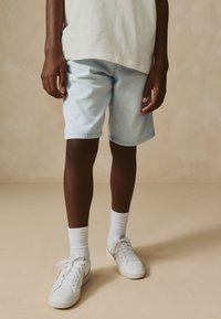 Light blue denim shorts with a relaxed fit, cuffed hems, paired with white sneakers and ribbed white socks. Simple, casual design.