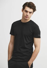 Czarny t-shirt z krótkim rękawem, wykonany z gładkiego materiału, z okrągłym dekoltem, szwem bocznym i subtelnym akcentem logo na lewym rękawie.