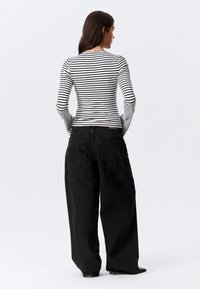 Stribet langærmet skjorte i sort og hvid kombineret med løse sorte jeans. Skjorten har rund hals og tætsiddende ærmer.