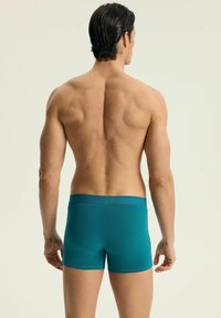 Teal męskie bokserki wykonane z gładkiego materiału, charakteryzujące się dopasowanym krojem i bezszwową talią. Widok z tyłu pokazuje gładką teksturę.