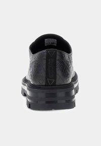 Scarpa nera low-top con motivo a logo in rilievo, suola spessa e scanalata, e linguetta con marchio sul tallone, mostrata da una vista posteriore.