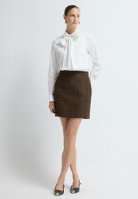 Witte blouse met een grote strik halslijn, een bruin tweed mini-rokje en zwarte puntige hakken met een gouden accent op de punt.