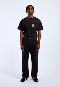 Black short-sleeve t-shirt with a graphic print on the chest, paired with high-waisted black jeans and black sneakers.