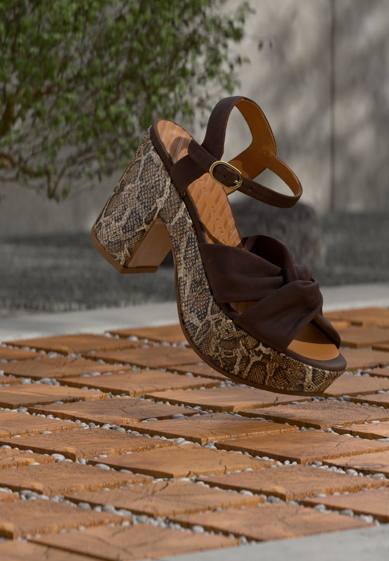 Καφέ σανδάλια με τακούνι, διακοσμημένα με υφή φιδίσιου δέρματος στο τακούνι και κορυφή από υφασμάτινο κόμπο σε καφέ χρώμα, με λουράκι με αγκράφα για ασφαλή εφαρμογή.