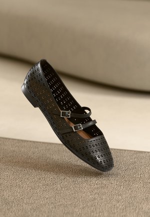 Schwarze, gelochte Ballerinas mit zwei verstellbaren Riemen und runder Zehenpartie, ausgestattet mit einem glatten Innenfutter und flacher Sohle.