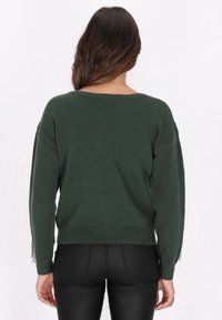 Pulover verde din tricot, cu o croială lejeră, guler larg și mâneci lungi. Prezintă un tiv cu nervuri și detalii texturate cu franjuri pe mâneci.
