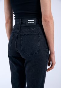 Svarta denimjeans med hög midja, med en patchlabel på baksidan och två bakfickor. Tyget har en lätt textur.