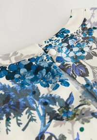 Gros plan d'un tissu avec un imprimé floral bleu et gris et deux boutons recouverts de tissu sur fond crème.