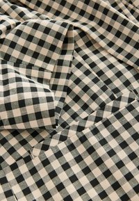 Svart och beige gingham tyg med ett rutmönster, tillverkat av texturerat material, vikt för att visa djup och dimensjonalitet.