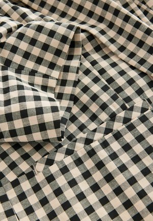 Crna i bež gingham tkanina s uzorkom rešetke, izrađena od teksturiranog materijala, presavijena kako bi prikazala dubinu i dimenzionalnost.