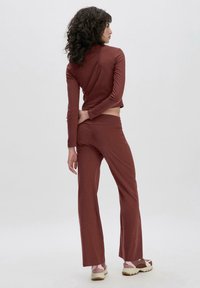 Bordeaux fijngebreide top met lange mouwen en een cropped ontwerp, gecombineerd met bijpassende strakke broek. De stof lijkt soepel, elastisch en lichtgewicht te zijn.