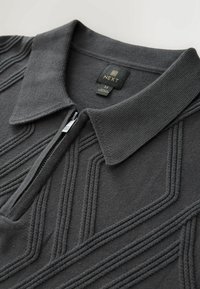 Sötétszürke cipzáras pólóing, texturált kötött mintával és klasszikus gallérral. Hímzett logó címke található a nyakrészen.
