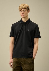 Polo nero con placca a due bottoni, colletto bianco a contrasto e piccolo logo sul lato sinistro del petto; realizzato in cotone morbido.