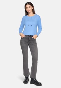 Jasnoniebieski sweter z długim rękawem, okrągłym dekoltem i sznurkiem, w połączeniu z szarymi dopasowanymi dżinsami i czarnymi botkami za kostkę.