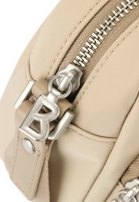 Angolo di borsa in nylon beige con zip argentata e hardware con logo. Presenta dettagli testurizzati e superfici lisce. Vista ravvicinata che mette in risalto i dettagli.