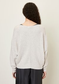 Svetlo sivi oversized pulover z mehkimi teksturami, spuščeni rameni in širokim ovratnikom, v kombinaciji z črno krilom. Brez vidnih vzorcev.