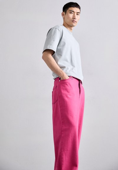 Ανοιχτό γκρι κοντομάνικο μπλουζάκι συνδυασμένο με φαρδιά φωτεινά ροζ παντελόνια που διαθέ�τουν τσέπη και λεπτομέρεια κουμπιού στη μέση.