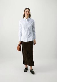 Balta mygtukų užsegimo palaidinė su ilgomis rankovėmis, derinama su rudą suede maksi sijoną. Modelis laiko rudą rankinę ir dėvi juodus loaferius.