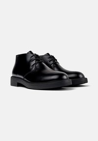 Par de botas de cuero negro con cordones hasta el tobillo, con puntas redondeadas y suelas de goma gruesa sobre un fondo blanco.