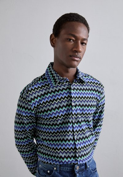 Μακρυμάνικη πουκάμισο με σχέδιο ζιγκ-ζαγκ σε αποχρώσεις του μπλε, του πράσινου και του μαύρου. Είναι κατασκευασμένο από απαλό ύφασμα με σχέδιο με κουμπιά.