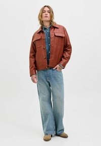 Brun læderjakke med store frontlommer og knaplukning, parret med denimskjorte og lyseblå brede bukser. Blød tekstur, afslappet stil.