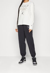 Weißes Langarmshirt mit "Nike Flight" Grafik, kombiniert mit schwarzen Jogginghosen mit einem Logo. Schwarze und graue High-Top Sneaker.