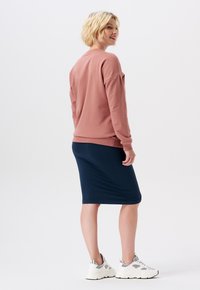 Sweatshirt en coton rose à manches longues, associé à une jupe côtelée bleu marine et des baskets blanches. La tenue présente une coupe décontractée et des détails subtils.