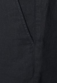 Schwarzer Leinenstoff mit strukturiertem Oberflächenbild und sichtbaren Nähten. Verfügt über eine Seitentasche, die ein lässiges, entspanntes Design unterstreicht.