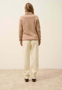 Suéter de mezcla de lana beige con un cuello alto, combinado con pantalones cremosos de corte holgado y zapatos de tacón cuadrado marrones. Diseño minimalista.