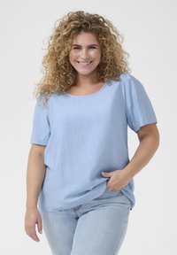Haut bleu clair à manches courtes en tissu texturé avec un col rond. Coupe décontractée, associé à un jean en denim bleu clair.