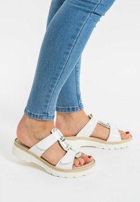 White platform sandals with textured sole, featuring two wide straps and metallic accents. Paired with blue skinny jeans.