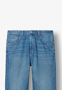 Gaiši zili džinsi ar taisnu piegriezumu, kuram ir pieci maciņi, metāla pogu aizdare un smalkas izbalēšanas detaļas.