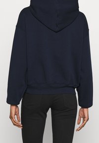 Felpa con cappuccio blu navy dal taglio rilassato, con polsini e fondo a costine, realizzata in tessuto morbido e con una texture liscia.