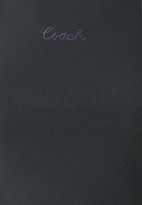 Svart ribbestrikket tank topp med det broderte merket "Coach" i en mørkere nyanse. Stoffet har en fin, teksturert overflate.