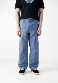 Lichtblauwe katoenen broek met een losse pasvorm, voorzien van een knoopsluiting en zijzakken, gecombineerd met zwarte schoenen en een grafisch T-shirt.