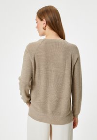 Beżowy sweter dzianinowy o luźnym kroju, z prążkowaną fakturą, raglanowymi rękawami i okrągłym dekoltem. Miękka tkanina, minimalne wykończenia.